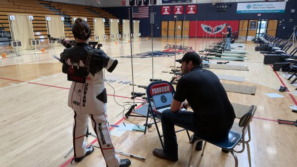 Coach Sahi Weiser (Left) practices her Precision Air Rifle Skills on the line with a SCAT trainer attached while watched and working with Coach Angus Babcock on target approach.